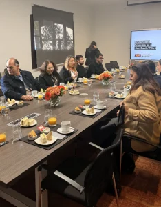 People seated around a long conference table with plates of sandwiches and glasses of orange juice during a meeting in a modern office.
