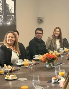 Group of people seated around a conference table with plates, juice, and sandwiches during a meeting or meal.