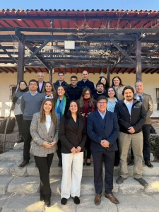 Group of about 20 professionals standing on stone steps under a wooden pergola, posing for a photo outdoors on a sunny day .