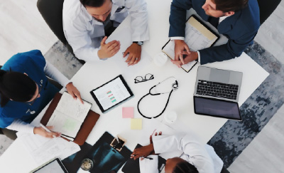 Top-down view of healthcare professionals collaborating around a table with a tablet showing charts, notebooks, and a stethoscope.